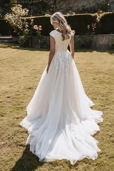 a woman standing in the grass wearing a wedding dress