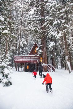 two children are skiing in front of a log cabin on a snow covered hill with pine trees