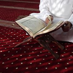 a man sitting down reading a book on a red carpeted area with white dots