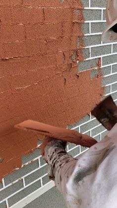 a person wearing a white hat and holding a paint roller in front of a brick wall