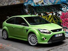 a green car parked in front of a graffiti covered wall