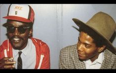 two men wearing hats and ties sitting next to each other in front of a wall