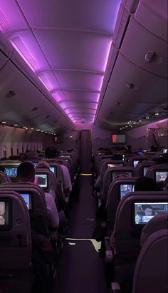 the inside of an airplane with purple lights and televisions on each side of the aisle