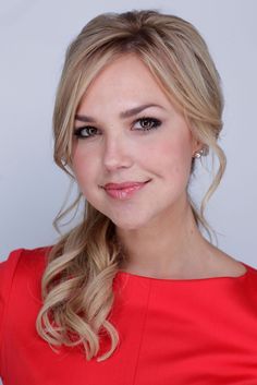 a woman in a red dress smiling at the camera with her hair pulled up into a braid