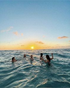 four people swimming in the ocean at sunset