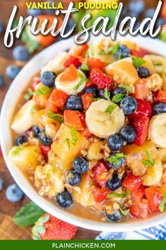 a white bowl filled with fruit salad on top of a wooden table next to blueberries and