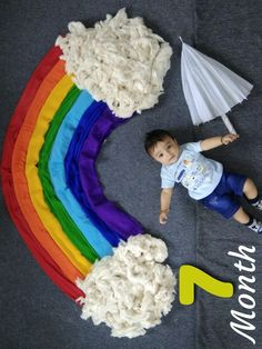 a young boy laying on the ground next to a rainbow cake with white frosting