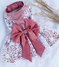 a pink and white dress with a bow on the front, sitting next to some flowers