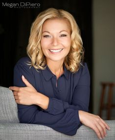 a woman sitting on top of a gray couch smiling at the camera with her arms crossed