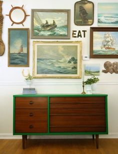 there are many paintings on the wall above this green dresser and sideboard with two vases