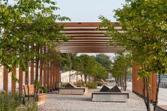 an outdoor seating area with benches and trees in the foreground, under a pergolated canopy