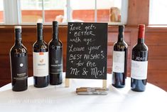 three bottles of wine sitting on top of a table next to a chalkboard sign