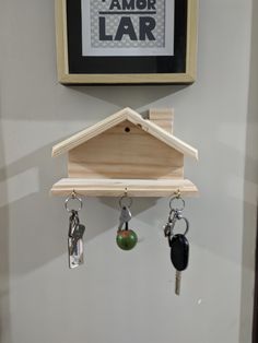 a bird house with keys hanging from it's hooks on the wall next to a framed poster