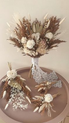 an arrangement of dried flowers in a vase sitting on a round metal tray with lace