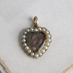 "Circa 1840 an antique Victorian heart-shaped locket charm crafted in 14k yellow gold featuring a beveled-glass covered compartment holding a beautifully woven love-knot of chestnut brown hair. With the pearl surround (likely natural pearls but not tested) set in cut-down collets and the back extravagantly chased in a lush acanthus leaf pattern and \"B. Hunter\" engraved on a ribbon banner, it's a poignant and rare example of early Victorian mourning jewelry. Measuring approximately 7/8\" north Victorian Heart Charm Pendant Jewelry, Victorian Jewelry With Heart Pendant And Charm, Victorian Jewelry With Heart Charm For Anniversary, Antique Yellow Gold Jewelry With Heart Charm, Victorian Heart-shaped Keepsake Jewelry, Victorian Heart Charms Jewelry, Victorian Heart-shaped Charms Jewelry, Victorian Jewelry With Heart Charm As Keepsake, Victorian Jewelry With Heart Charm For Keepsake