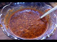 a glass bowl filled with chili sauce on top of a wooden table next to a knife