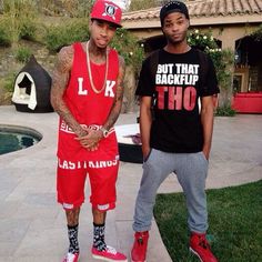 two young men standing next to each other in front of a pool wearing matching outfits