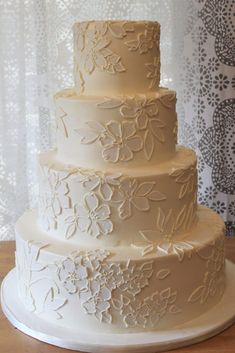 a three tiered white wedding cake sitting on top of a wooden table next to a window