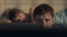 two people laying on a bed with one man looking at the camera and the other is staring