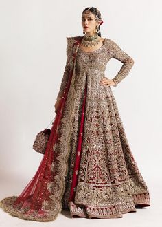 a woman in a red and gold bridal gown standing against a wall with her hands on her hips