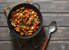 a skillet filled with lentils and vegetables on top of a wooden cutting board