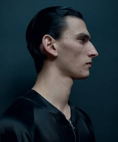 a man with dark hair and black shirt looking off to the side in front of a dark background