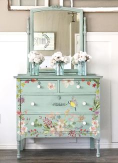 an old dresser with flowers painted on it and a mirror above the drawers is shown