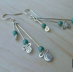 two pairs of silver and green beads are hanging from earrings on a wooden surface,