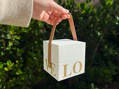 a person holding a white box with the word love on it in front of some bushes