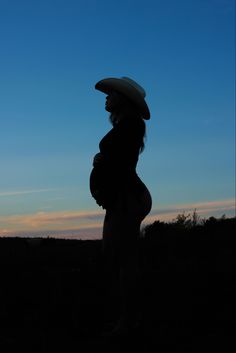 the silhouette of a pregnant woman with a hat on her head is seen against a blue sky