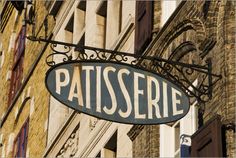 the sign for patisserie is hanging from the side of an old building