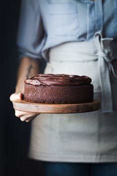 a woman holding a chocolate cake on a wooden platter