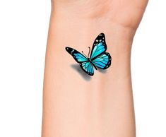 a blue butterfly tattoo on the wrist is shown in close up, it appears to be flying