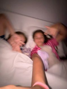 two people laying in bed with one pointing at the camera and the other holding their hand up