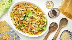 a salad with chicken, lettuce and carrots in a white bowl next to wooden utensils