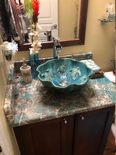 a bathroom sink sitting on top of a counter next to a mirror with flowers in it