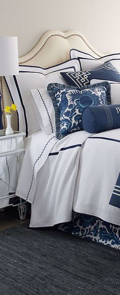 a bed with blue and white comforters on top of it next to a night stand