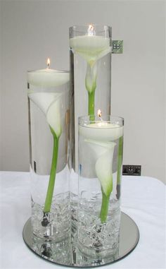 two tall vases with flowers in them on a table next to some water and candles