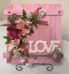 a pink wooden sign with flowers and hearts hanging from it's sides on a white table