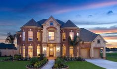 a large brick house with lots of windows and landscaping in front of it at dusk