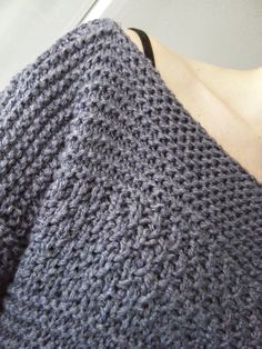 a close up of a person wearing a gray knitted shawl with holes in the middle