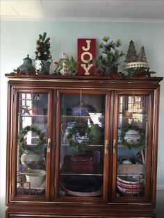 an old china cabinet with christmas wreaths and other holiday decorations on the top shelf