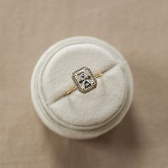 an engagement ring with a diamond in it sits on a white cloth covered box that is sitting on the floor