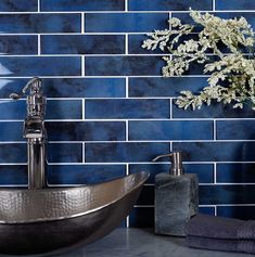 a bathroom with blue tiles and a sink in the middle, next to a vase with white flowers