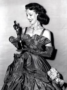 an old black and white photo of a woman in a ball gown holding her oscar award