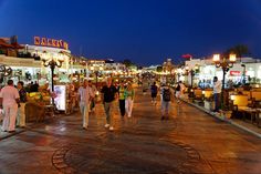 many people are walking down the street in front of shops and restaurants at night time