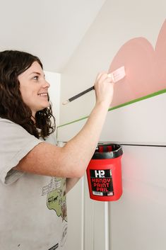 a woman is painting a wall with pink hearts on it and holding a paintbrush