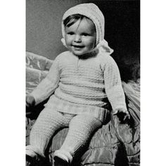 black and white photograph of a baby sitting on a bed wearing a knitted outfit