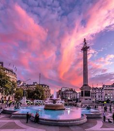 people are standing in front of a fountain with a pink and blue sky behind it