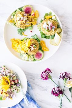 two white plates filled with food on top of a marble table next to purple and yellow flowers